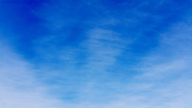Deep blue sky backing shot with white clouds. Clean cloudscape space with just a interweave cloud to use as a background in your designing  area. Royalty free stock photo.