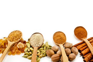 Nutmeg, cinnamon, cardamom, brown sugar and powder of nutmeg, cinnamon, cardamon, brown sugar in a wooden spoons isolated on white background. Text space.
