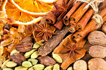 Slices of dried orange, brown sugar crystals, cardamom, nutmeg, cinnamon sticks and star anise on wooden background. Sweet spices background.