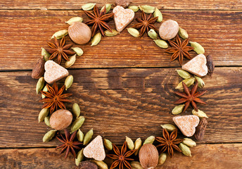 Christmas wreath made of spices. Star anise, nutmeg, green cardamom and hearts of sugar on wooden background. Top view. Copy space, Greeting card.
