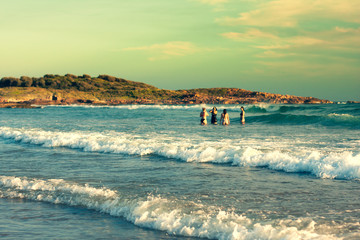 Fore women are swimming in the ocean, standing in the waves. Greenish sky and water. The ocean is...