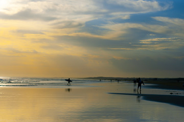Obraz premium A narrow strip of ocean water, a large sky space and the reflecting wet sand of the beach in blue and yellow. Some people in the distance, a man with a surfboard. Anna Bay, Australia