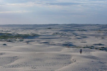 Large open desert empty space with blue sand waves. Chain tracks and a lonely man in the foreground. Stockton Sand Dunes near the coast, Worimi Regional Park, Anna Bay, Australia