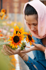 Vertical photo. A girl in a scarf sniffs sunflowers. Parishioner of the church. The concept of nature and man. A woman neatly holds flowers to the bush.