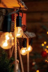 Glowing light bulbs of a garland hanging on shelves of wood, braided ropes and Christmas tree. New Year and Christmas decor.