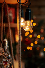 Glowing light bulbs of a garland hanging on shelves of wood, braided ropes and Christmas tree. New Year and Christmas decor.