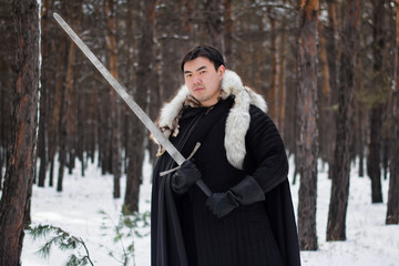A warrior in black quilted clothes in a black cloak with a white fur collar and a long sword in his...