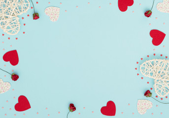 Valentine's Day blue background with rattan and felt hearts, red roses and small red and pink hearts. Greeting, invitation card. Wedding, love, happiness concept. Flat lay, top view with copy space.