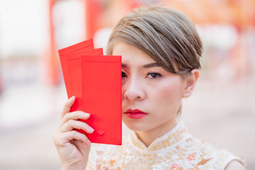 Close-up of Asian women wearing cream-colored Chinese outfits and showing a red envelope on the...