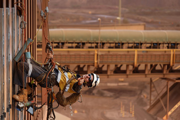 Happy rope access welder worker wearing fully safety harness equipment abseiling and resting in...