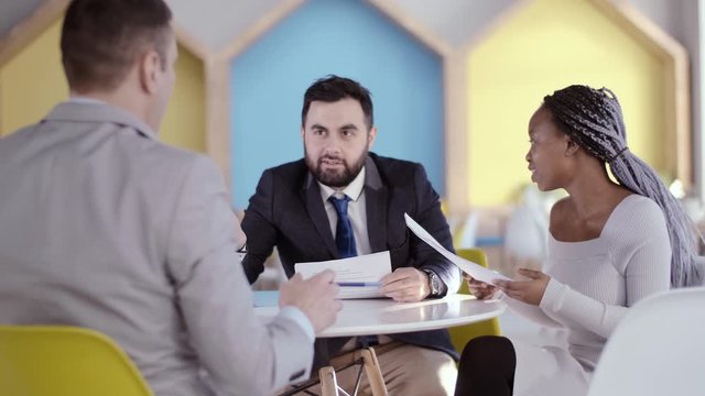 Three businessmen of different races at the negotiating table, study documents before signing a new contract. A young African American business woman speaks to her opponent through her human