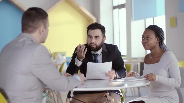 A young African American business woman at the negotiating table tells her business partner, with the help of her translator, that she agrees to the proposed conditions. Business partners shake hands.