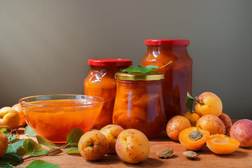Apricot jam in a glass dish and jars. Fresh ripe apricots with leaves on the table. Homemade confiture.