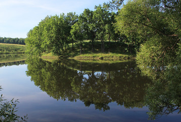 Fototapeta premium A pond with a winding Bank and the reflection of trees in the water around.