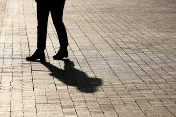 Silhouette and shadow of woman walking down on a street, side view. Concept of loneliness, parting, dramatic stories, human life