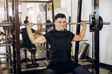 Fototapeta na wymiar Sports man in the gym. A man performs exercises. Guy in a black t-shirt
