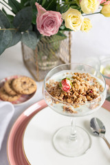 Light granola with Greek yogurt in a glass goblet on a porcelain dish on a white tablecloth.