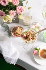 Breakfast concept, Sunday brunch in a restaurant. Light granola with Greek yogurt in a glass goblet, coffee, light sweets and flowers on a snow-white tablecloth.