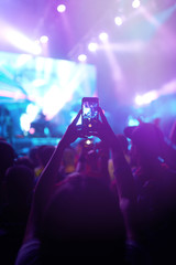 Hand with a phone records live music festival. People taking photographs with smart phone during a...