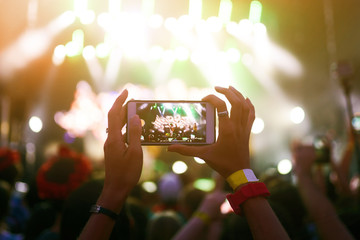 Hand with a phone records live music festival. People taking photographs with smart phone during a...