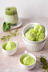Balls of vegetarian ice cream with matcha tea in white porcelain dishes and in white cups on a light background. Vertical image and close-up