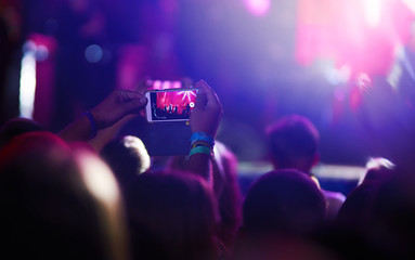 Fototapeta na wymiar Hand with a phone records live music festival. People taking photographs with smart phone during a public music concert. Crowd raising their hands, dancing and enjoying great the concert.