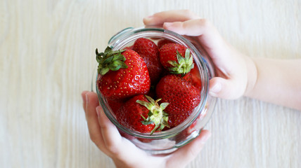children's hands hold a glass jar with large bright juicy red berry strawberries