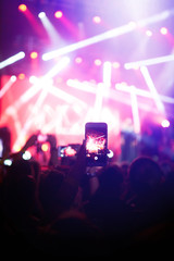 Hand with a phone records live music festival. People taking photographs with smart phone during a...