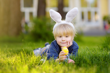 Pretty little boy wearing bunny ears hunting for easter eggs in spring park on Easter day.