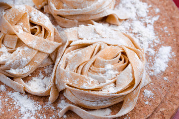 Uncooked fettuccine nest with flour on wooden board. Tasty fresh ingredients for cooking pasta. Plaid background