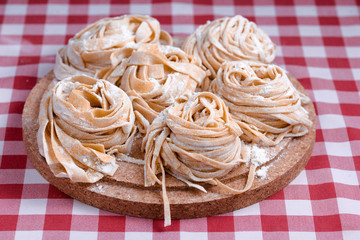 Uncooked fettuccine nest with flour on wooden board. Tasty fresh ingredients for cooking pasta. Plaid background