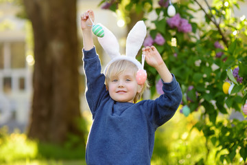 Pretty little boy wearing bunny ears hunting for easter eggs in spring park on Easter day.