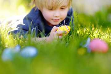 Little boy hunting for easter egg in spring garden on Easter day. Focus on multicolor eggs.