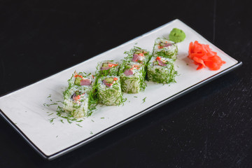 Salmon sushi rolls served on a white plate with ginger and wasabi sauce in a restaurant on table. Japanese cuisine.