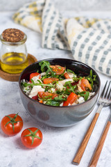 Salad with chicken, tomatoes and spinach with Peking cabbage in a dark bowl with a napkin and butter on a light background