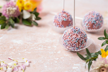 Chocolate popcake cake in the form of a popsicle close-up view with pink and yellow spring flowers on a marble background.