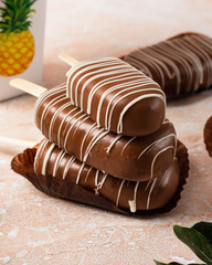 Chocolate popcake cake in the form of a popsicle close-up view with pink and yellow spring flowers on a marble background.