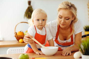 Happy mother and little daughter cooking in kitchen. Spending time all together, family fun concept