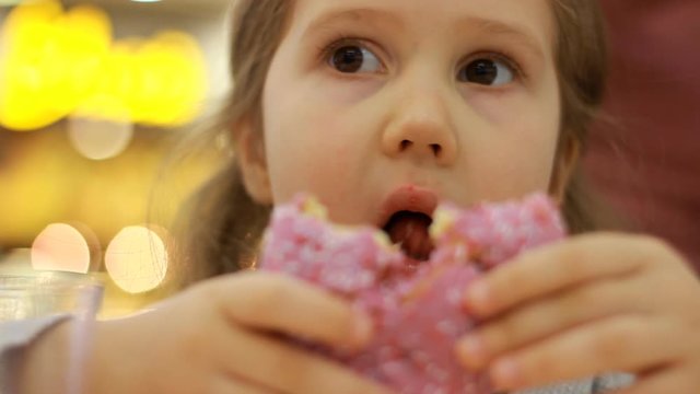 Child mouth bites rose donut. Closeup baby girl eating doughnut with glase. Delicious, sweet, sweettooth