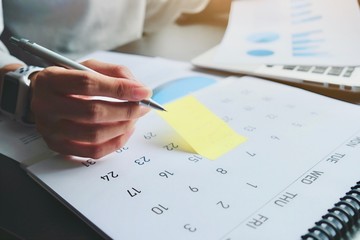 Asian woman is writing on yellow paper notes and put a warning on calendar. The other hand hold the...