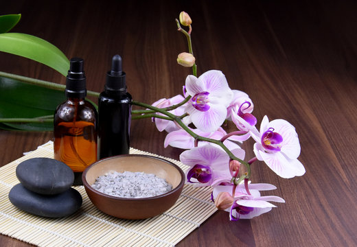 Spa and wellness setting with cosmetic phials stock images. Black massage stones with pink orchid stock images. Spa-concept with zen stones, purple orchid flower, brown cosmetic bottles and bath salt