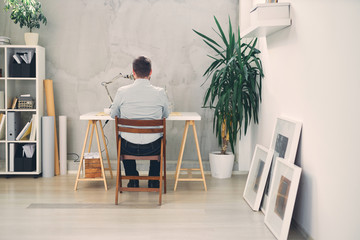 Back view of an young male architect sitting at his desk and typing.