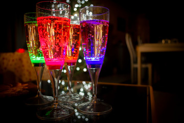 Colorful party glasses, red, blue and green, filled with champagne, cava or prosecco, on a dark and black background. Ready for bubbles and celebration. 