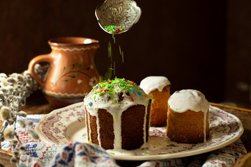 Decoration process of orthodox easter cake by sprinkling colorful sugar drops on icing tops od pastry. Cooking easter dish in orthodox traditions 