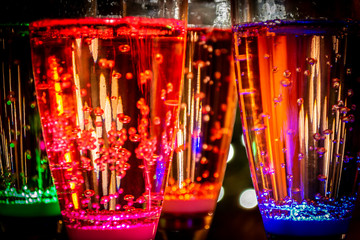 Colorful party glasses, red, blue and green, filled with champagne, cava or prosecco, on a dark and black background. Ready for bubbles and celebration. 