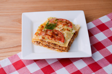 Traditional Italian lasagna made with minced beef, bolognese sauce, topped with basil leaf served on a white plate