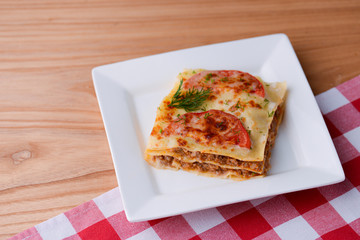 Traditional Italian lasagna made with minced beef, bolognese sauce, topped with basil leaf served on a white plate