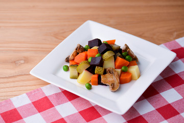 Vegetable stew salad with carrot, pickles, green beans, mushrooms and beetle served in a white plate over wooden table.