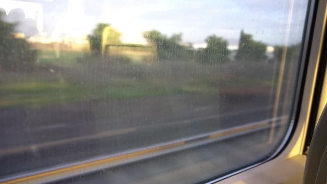 Industrial area with trees and big building from a train window, with reflection of sunset