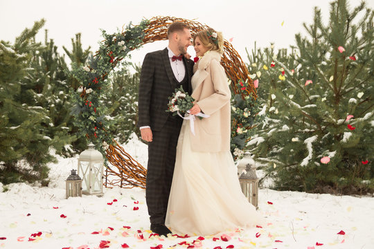 the couple is hugging and close to the kiss, holding hands, a bouquet in their hands. A suit with a butterfly and a coat with a dress. The bride and the groom
